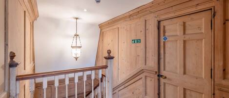 A wooden staircase with a white railing, a hanging light fixture, and a door with a fire exit sign.