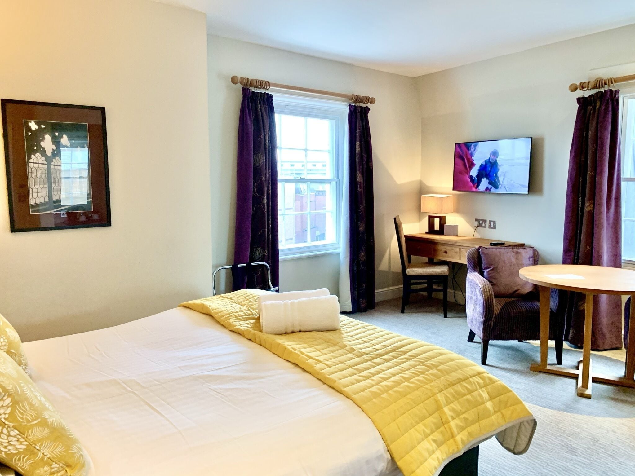 A hotel room with a bed, a desk, a chair, a TV, and a window with curtains.