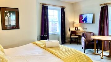 A hotel room with a bed, a desk, a chair, a TV, and a window with curtains.