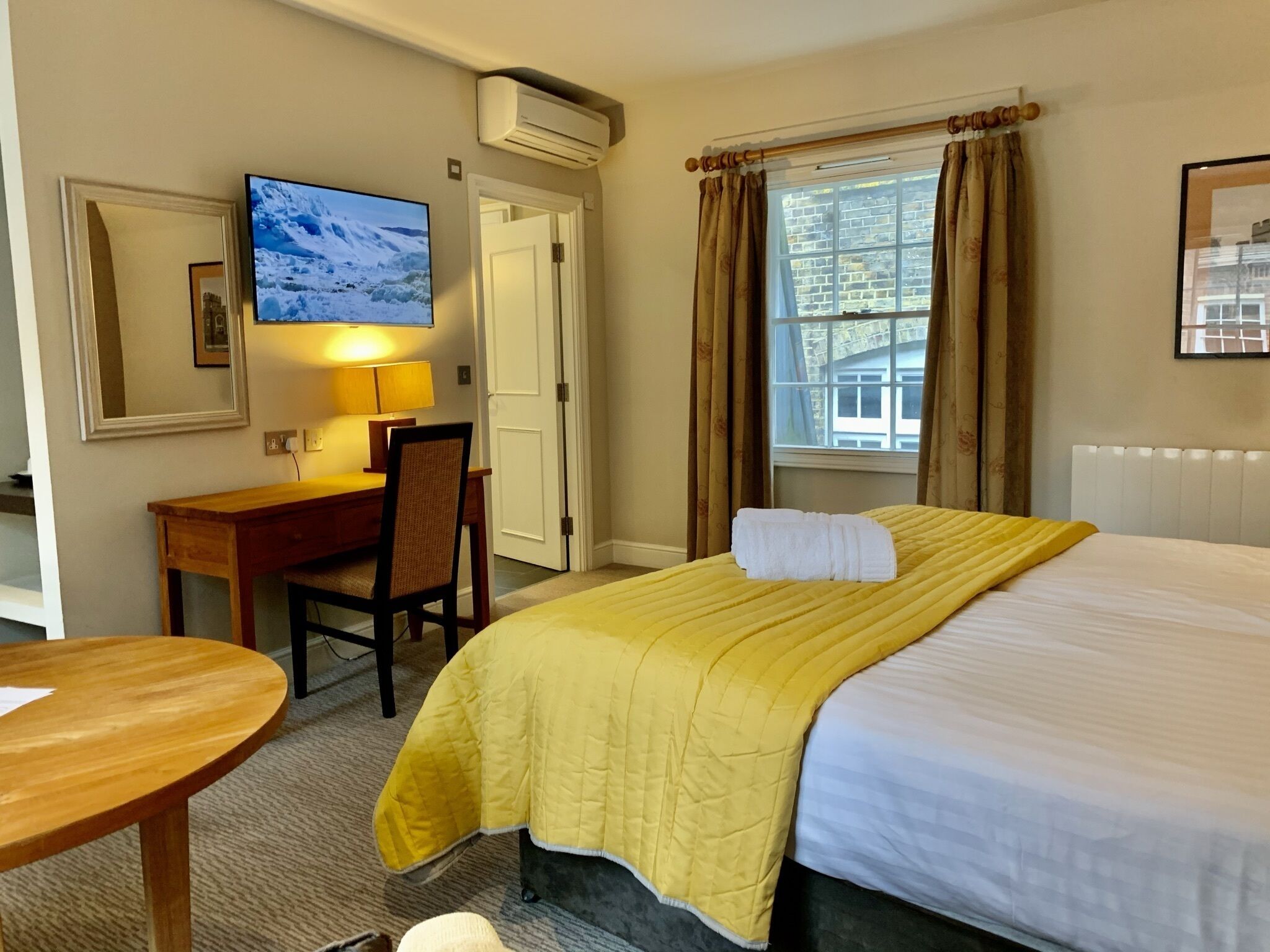 A hotel room with a bed, a desk, a chair, a TV, and a window with curtains.