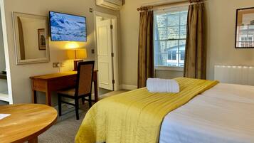A hotel room with a bed, a desk, a chair, a TV, and a window with curtains.