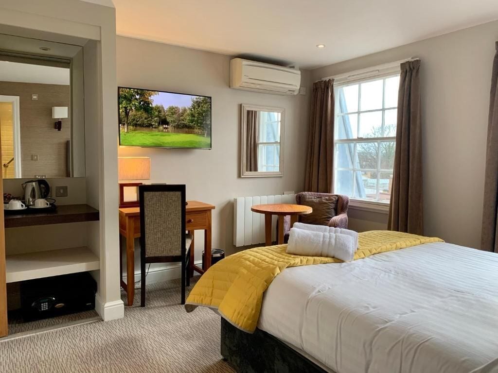 A hotel room with a bed, a desk, a chair, a TV, and a window.