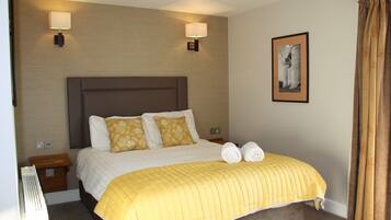 Quarto de hotel com uma cama grande, duas luminárias fixadas na parede, um quadro emoldurado e uma cortina.