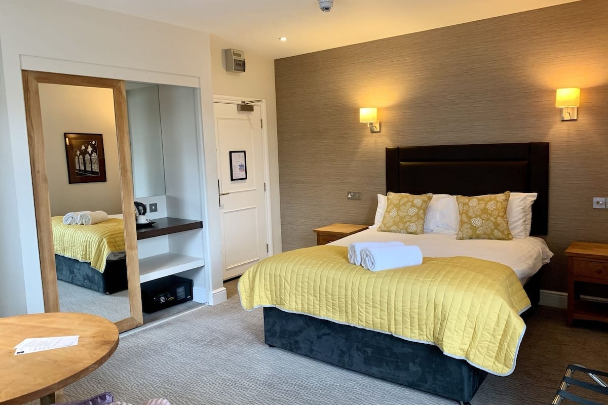 Quarto de hotel com uma cama grande, mesas de cabeceira, um espelho, uma mesinha e uma cadeira.