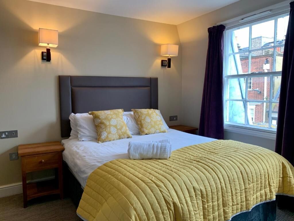 Habitación de hotel con cama, dos lámparas de noche, ventana con cortinas y vistas a edificios.