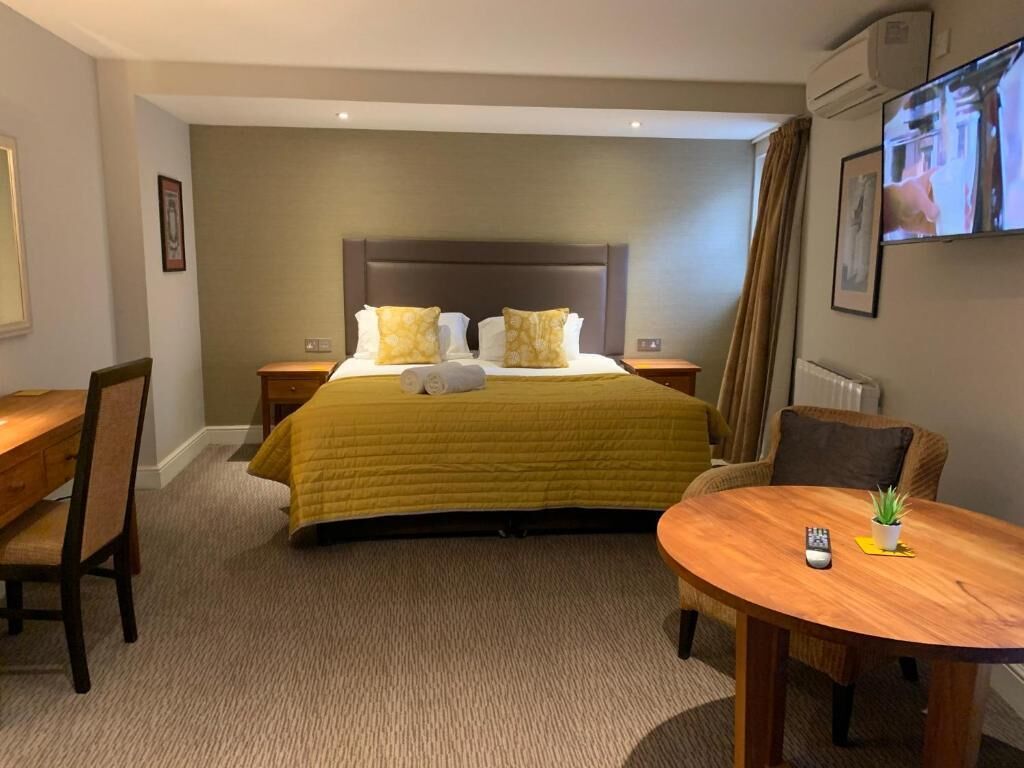 Una habitación de hotel con una cama grande, un escritorio, una silla, una mesa redonda con una planta y un televisor en la pared.