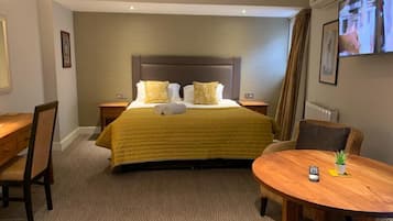 Una habitación de hotel con una cama grande, un escritorio, una silla, una mesa redonda con una planta y un televisor en la pared.