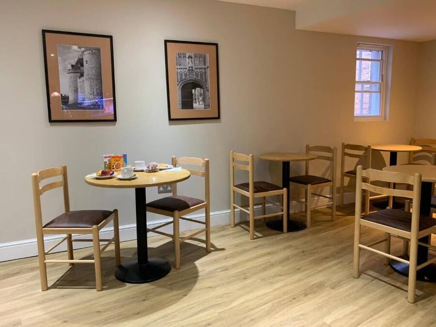 Een eethoek met houten stoelen en tafels, ingelijste foto's aan de muur en een raam.