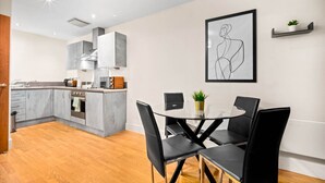 Uma cozinha moderna com armários cinza, uma ilha central e um espaço de jantar com cadeiras pretas e mesa de vidro.