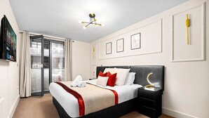 Quarto de hotel com cama, mesa de cabeceira, televisão fixada na parede e porta para uma varanda.