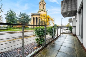 A balcony with a metal railing overlooking a street with a historic building and trees in the background. - Stylish City Centre Apartment -  Terrace - Netflix (West Midlands)