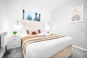 Un dormitorio moderno con una cama grande, pared de ladrillo blanco y una obra de arte enmarcada.