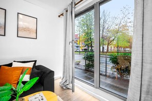 Una sala de estar moderna con un sofá negro, una mesa de centro y un amplio ventanal que ofrece vistas a la calle y árboles.
