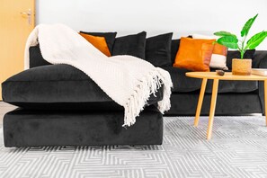 A black sofa with a white throw blanket, a small round wooden table with a plant, and a patterned rug. - Stylish City Centre Apartment -  Terrace - Netflix (West Midlands)