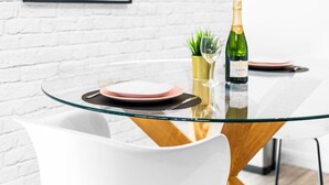 Un'area pranzo moderna con tavolo in vetro, sedie bianche e una bottiglia di CAVA.