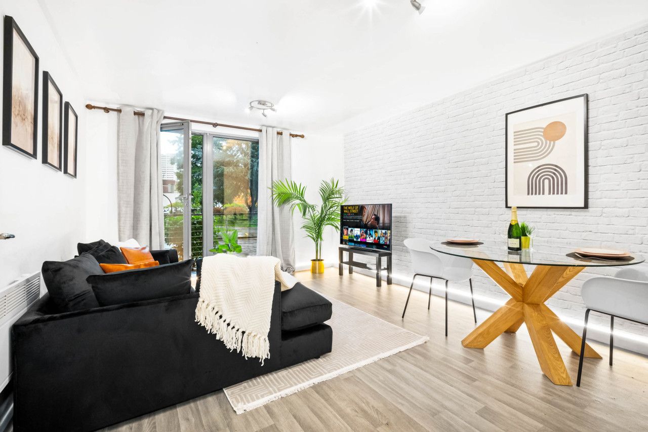 Una sala de estar moderna con un sofá negro, una mesa de centro de vidrio y una pared de ladrillo blanco.