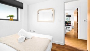 A modern hotel room with a bed, a large mirror, and a view into the kitchen area. - Birmingham City Centre Apartment - SuperHost
 (Birmingham)