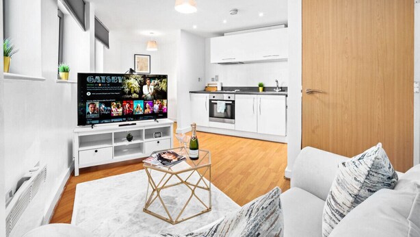 A modern living room with a flat-screen TV, a white sofa, a coffee table with a magazine, and a wooden door. - Birmingham City Centre Apartment - SuperHost
 (Birmingham)