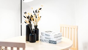 A round table with three books titled 'Vogue', 'Vogue', and 'Politics Today'. There are black vases with dried plants on the table. - Birmingham City Centre Apartment - SuperHost
 (Birmingham)