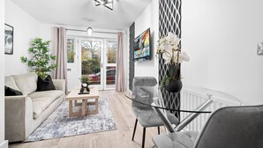 Ein modernes Wohnzimmer mit einer Couch, einem Couchtisch, Stühlen, einem Glastisch und einem Blumentopf.