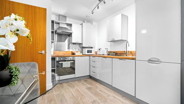 Una cocina moderna con armarios blancos, encimera de madera y horno empotrado.