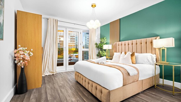 Ein modernes Hotelzimmer mit einem großen Bett, einem Holzschrank, einer Topfpflanze und Blick auf die Stadt durch die Glastür.
