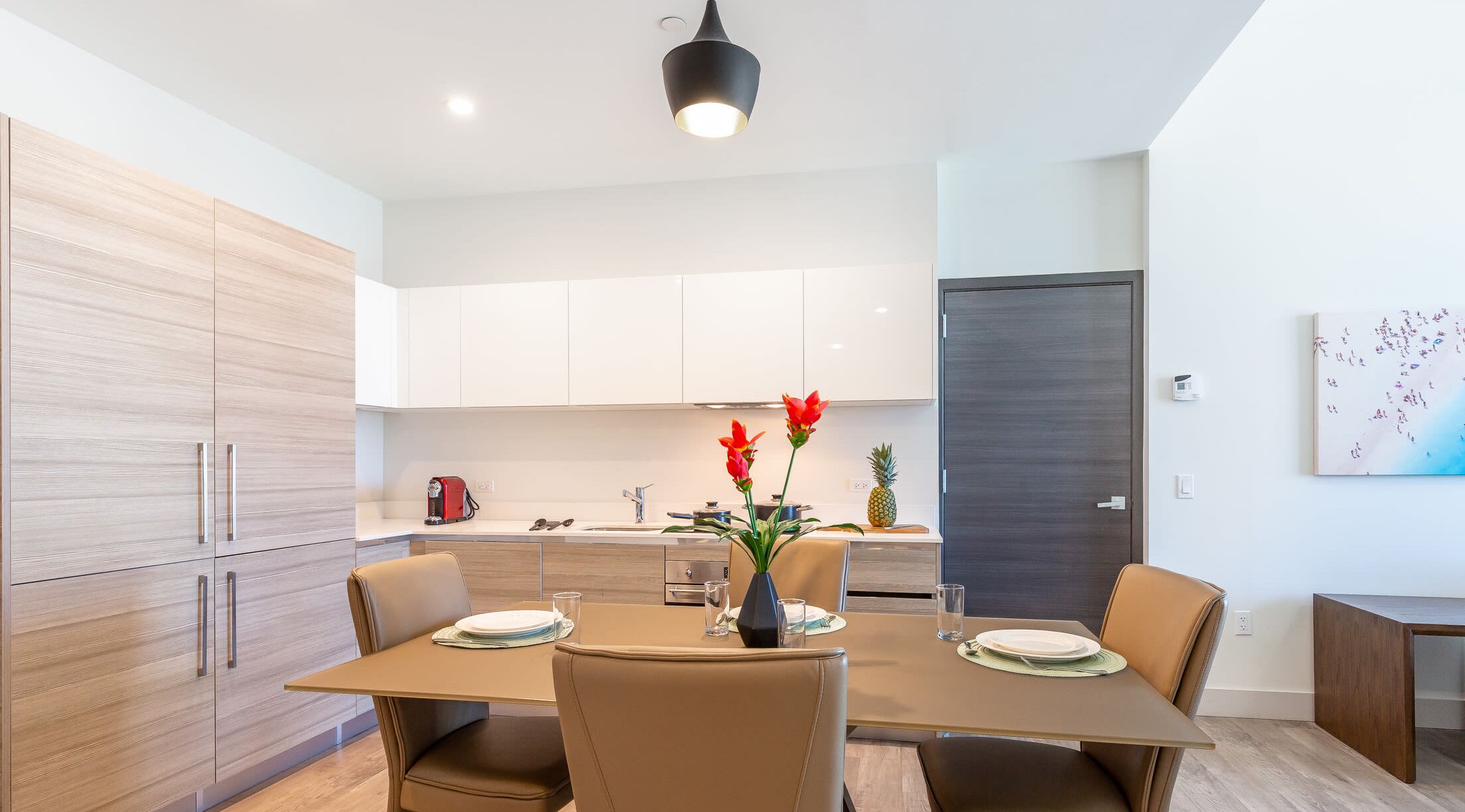 A modern kitchen with white cabinets, a dining table set for four, and a coffee machine.