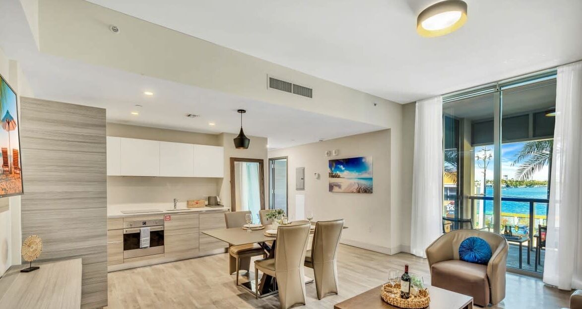 A modern kitchen with a dining area, large windows with a view of the sea, and a balcony with outdoor seating.