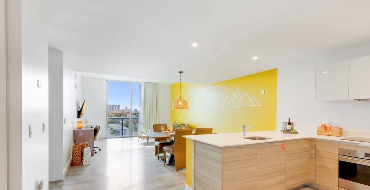 A modern kitchen with a yellow accent wall, wooden cabinets, and a large island with a sink.