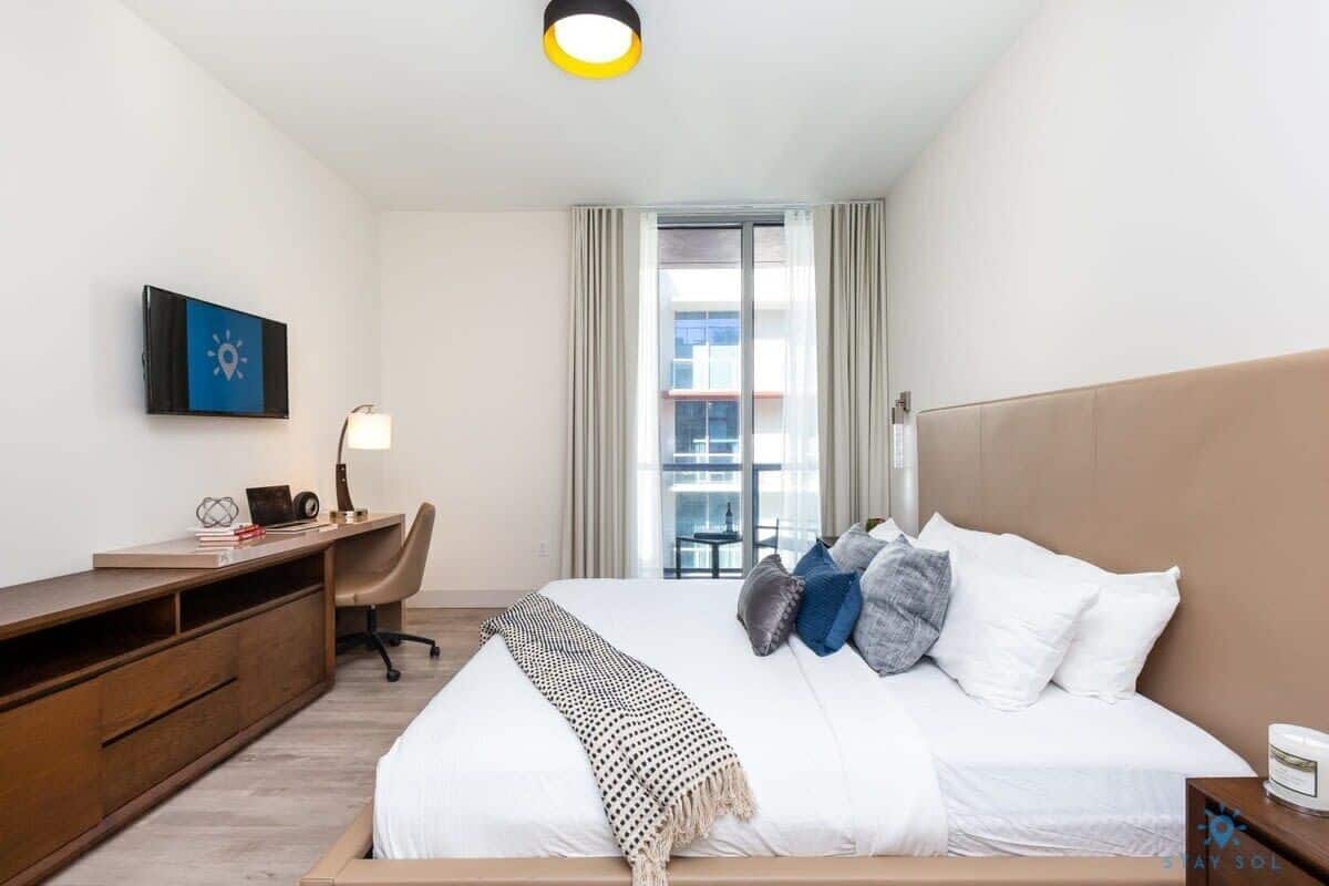 A hotel room with a bed, a desk, a chair, a TV, and a window with curtains.