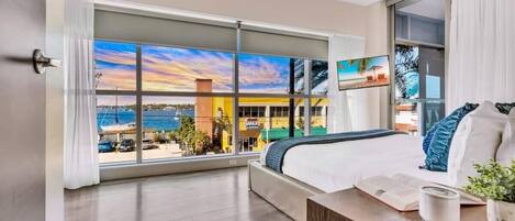 A hotel room with a large window offering a view of the beach and a building across the water.