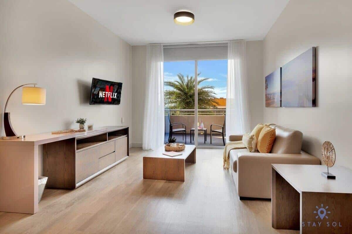 A modern living room with a TV, a sofa, a coffee table, and a balcony with a view.