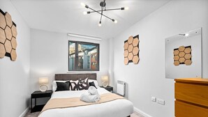 Ein modernes Schlafzimmer mit einem großen Bett, einer Holzkommode, einem Fenster mit Stadtblick und sechseckigen Wandverzierungen.