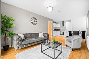 A modern living room with a grey sofa, a coffee table, and a dining area with a grey chair. - Luxury 2 Bedroom JQ Apartment (Birmingham)