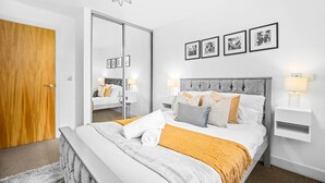 A modern bedroom with a large bed, a wooden door, a mirror, and framed pictures on the wall. - Cutlass Suite - Broad Street - Parking (West Midlands)