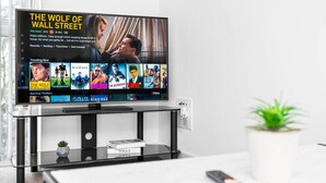 A flat-screen TV on a black stand with a remote control on a white table. - Cutlass Suite - Broad Street - Parking (West Midlands)