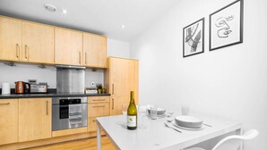 A modern kitchen with wooden cabinets, stainless steel appliances, and a white dining table set with glasses and a bottle. - Cutlass Suite - Broad Street - Parking (West Midlands)
