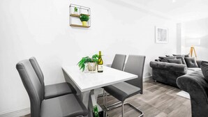 En moderne stue med en grå sofa, et hvidt spisebord med fire stole og en lille plante på væggen.
