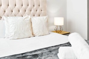 A neatly made bed with a tufted headboard, two pillows, and a bedside table with a lamp.