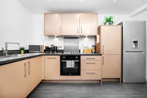 A modern kitchen with light-colored cabinets, a stainless steel refrigerator, and a built-in oven.
