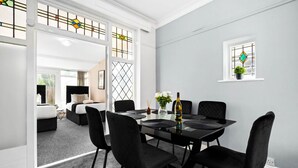 Un comedor con una mesa negra, sillas negras y una botella de vino. Se ve una ventana y una planta en la pared.