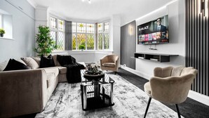 Una sala de estar moderna con un sofá color beige, una mesa de centro redonda y un televisor en la pared mostrando la interfaz de Netflix.