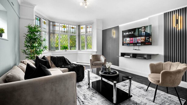 Una sala de estar moderna con un sofá, sillones, una mesa de centro, un televisor y un amplio ventanal con vidrieras.