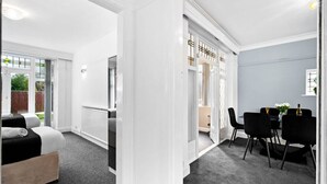 Habitación de hotel con cama, zona de comedor con sillas y vistas al exterior a través de un ventanal.