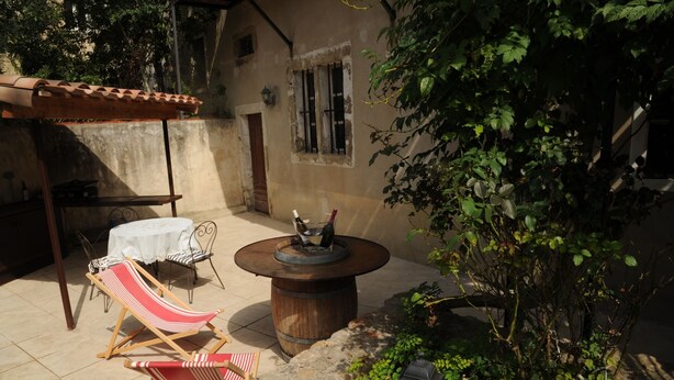 A patio with two striped lounge chairs, a round wooden table with a decorative item, and a small table with a white tablecloth. - Classic France Double:AC, BBQ, fresh&clean, garden (Limoux)