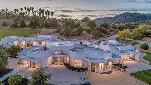A modern, multi-level house with a spacious patio and large windows, surrounded by a landscaped garden and a view of hills and power lines. - Avila Beach Estate: Exceptional Hope Ranch (San Luis Obispo)