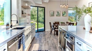 A modern kitchen with a large island, built-in appliances, and a dining area with a view. - Avila Beach Estate: Exceptional Hope Ranch (San Luis Obispo)