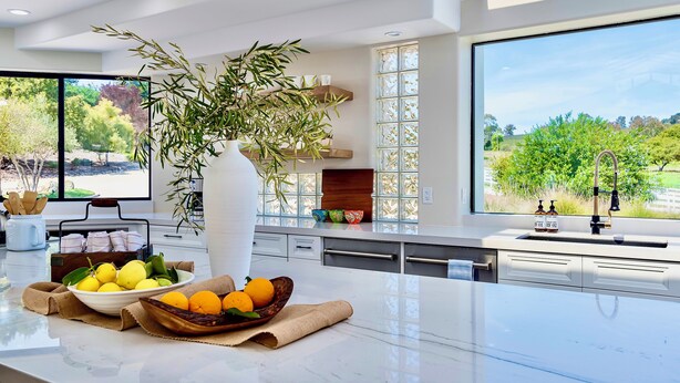 A modern kitchen with a large window, a bowl of fruit, and a potted plant. - Avila Beach Estate: Exceptional Hope Ranch (San Luis Obispo)