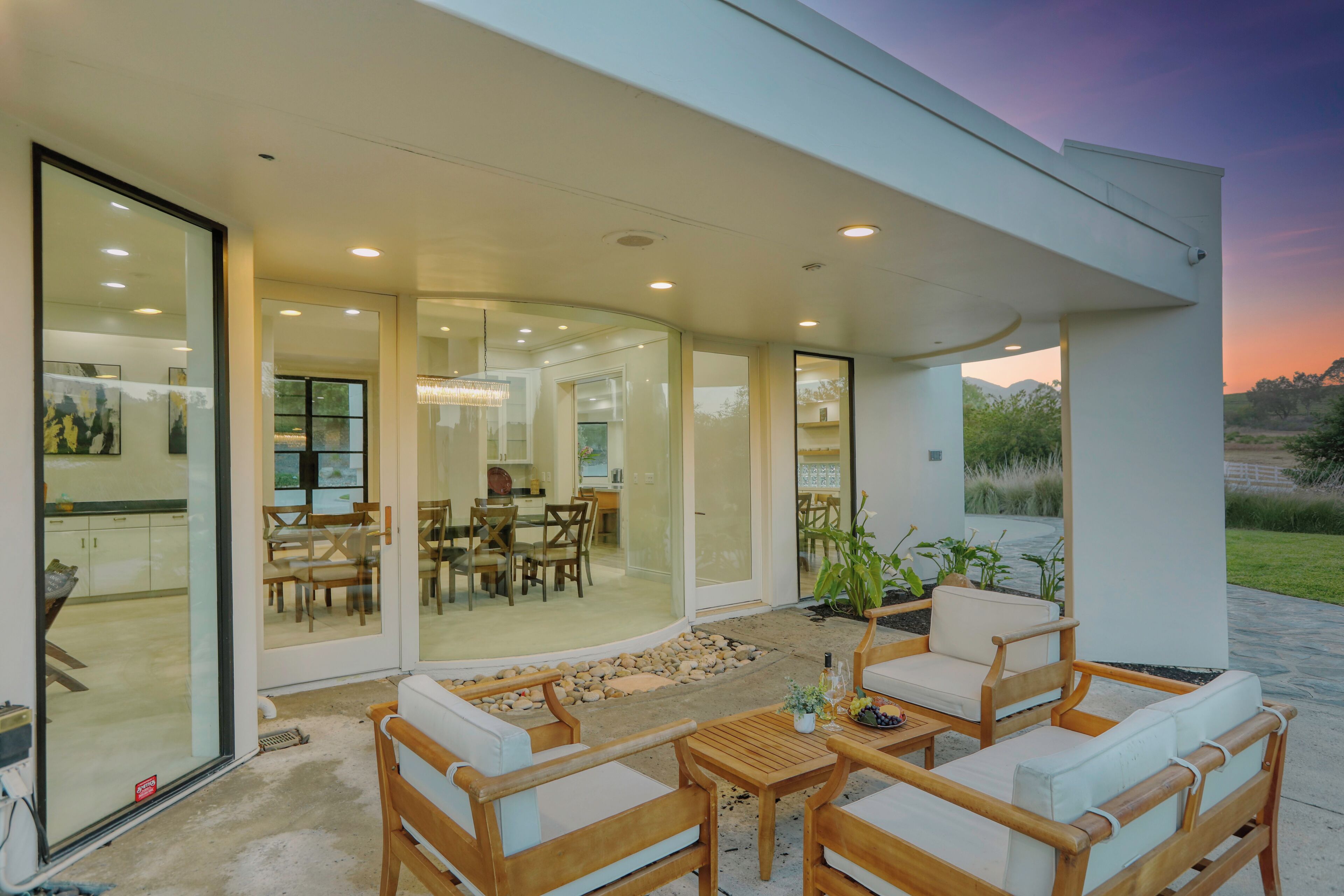 A modern outdoor patio with wooden furniture and a glass door leading to an interior dining area.