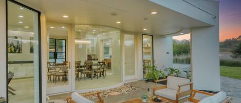 A modern outdoor patio with wooden furniture and a glass door leading to an interior dining area.